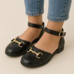 These are black leather Mary Jane shoes designed for girls, featuring a stylish gold horsebit detail across the front