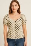 This cream polka dot blouse features a sweetheart neckline, puff sleeves with ruffled edges, and front button detailing