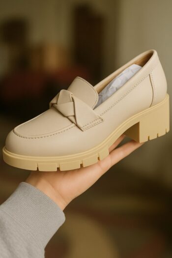 This is a stylish beige loafer featuring a chunky heel and a woven leather strap detail across the vamp