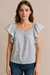 This light blue ruffled blouse features delicate textured embroidery and a gathered neckline