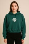This is a forest green cropped hoodie featuring a small white rose emblem centered on the chest. It has a relaxed fit with long sleeves