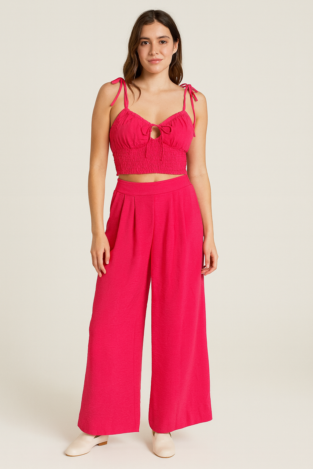 A vibrant three-piece pink set featuring wide-leg pants, a smocked crop top with tie straps,